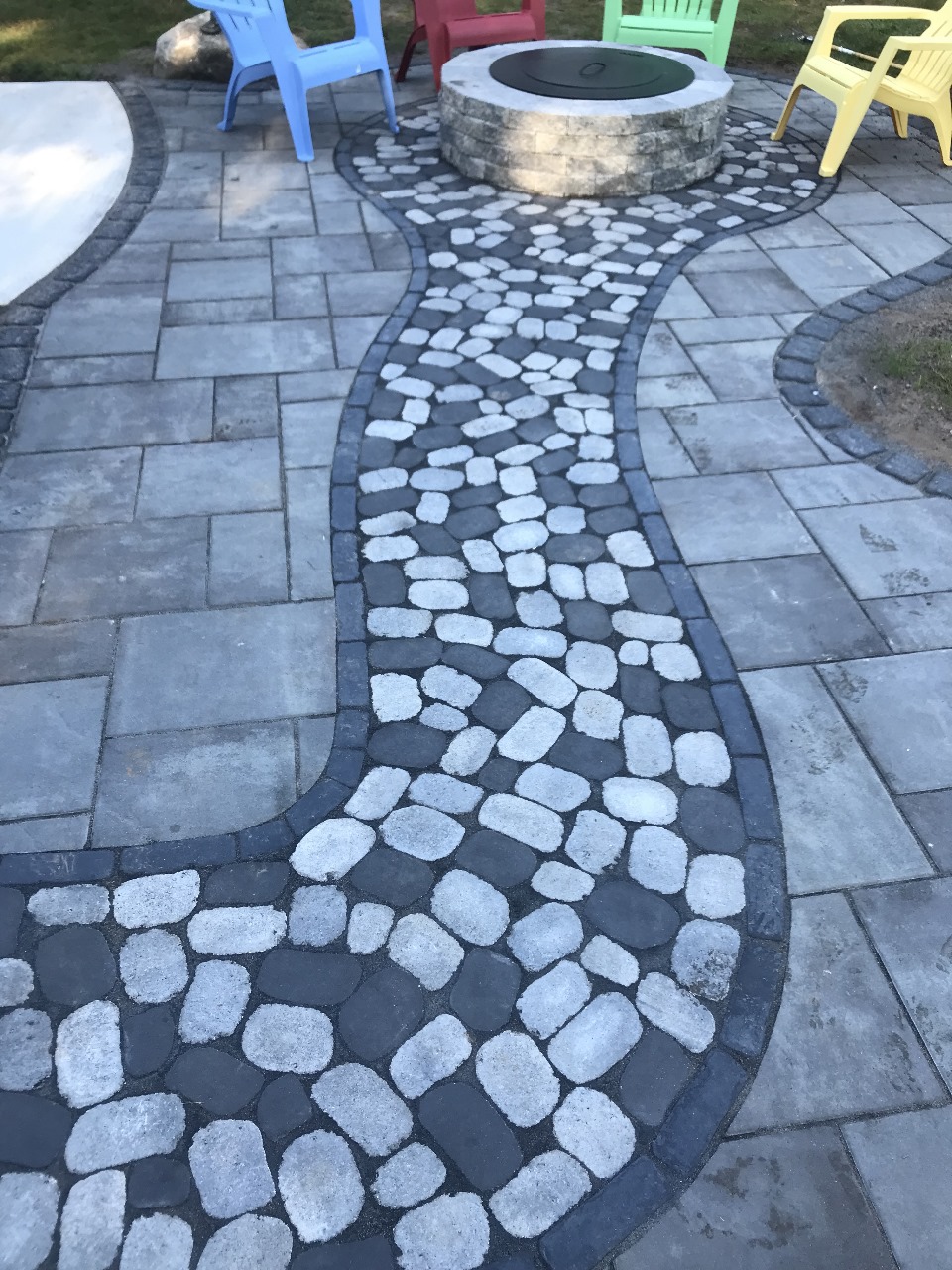 Paver patio with a pebble walkway leading to a stone fire pit