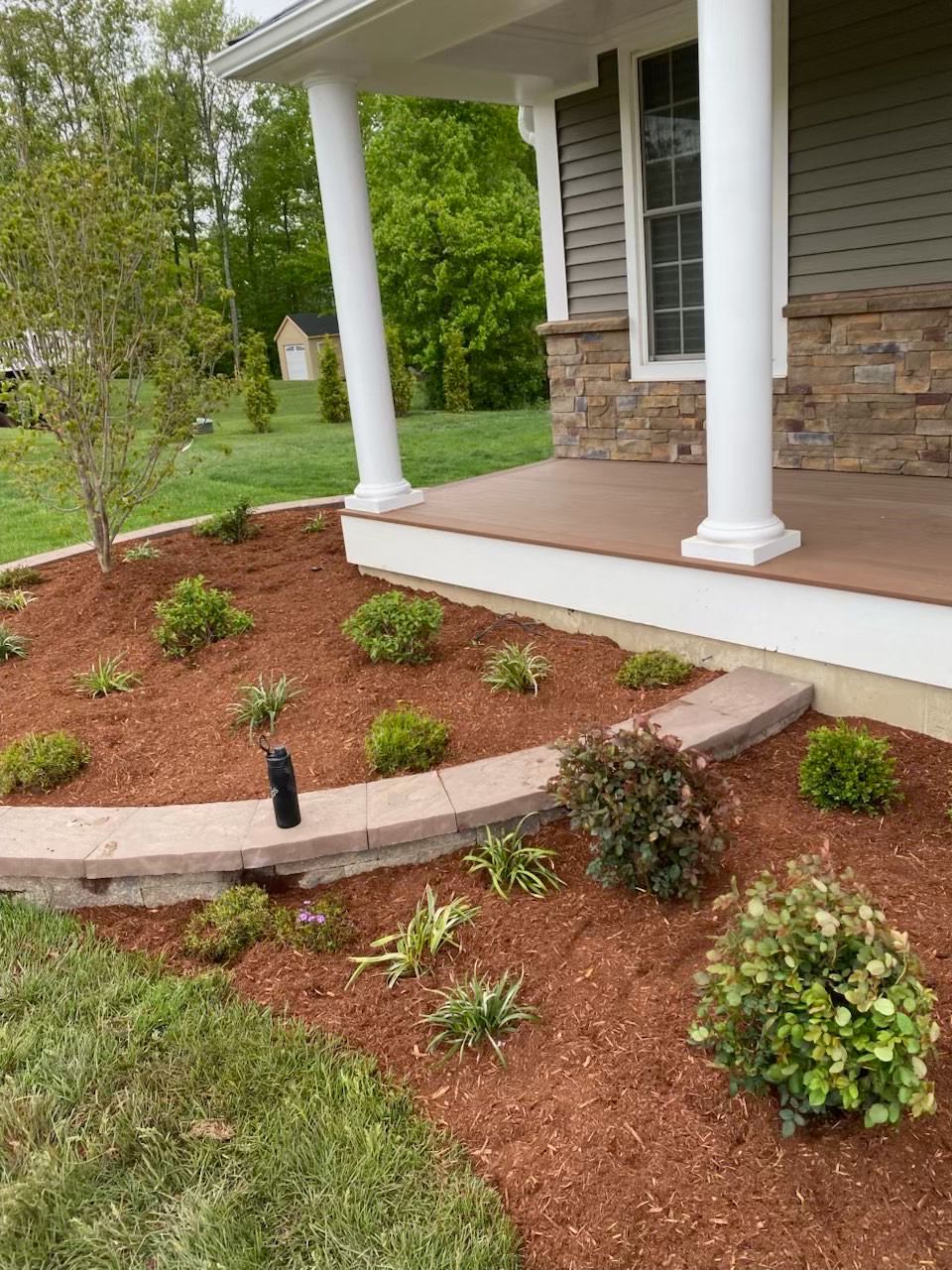 Mulched foundation planting and a low stone border along a porch